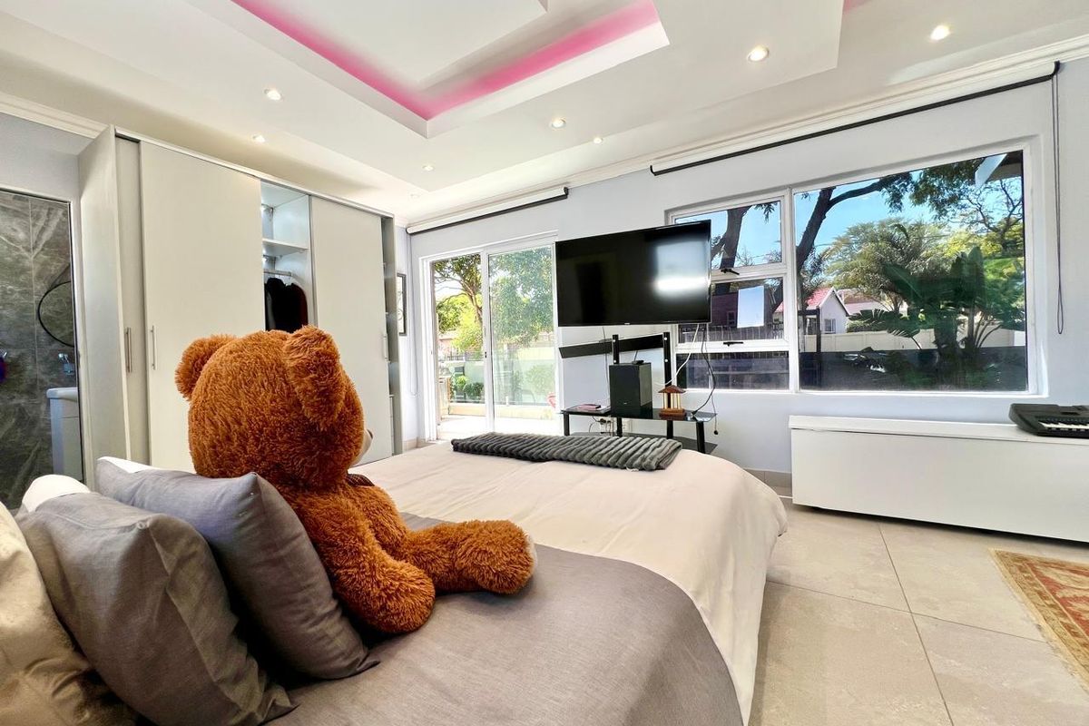 A modern bedroom featuring built-in wardrobes, recessed ceiling lighting with ambient accents, and large sliding glass doors providing ample natural light.