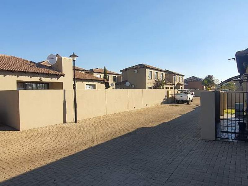 A view of the paved driveway and boundary wall leading to the townhouse entrance within the residential complex.