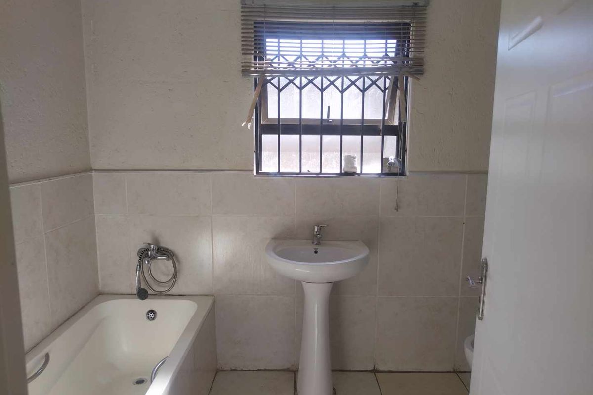 A functional bathroom featuring a pedestal basin, built-in bathtub, and neutral wall and floor tiling, ready for a modern update.