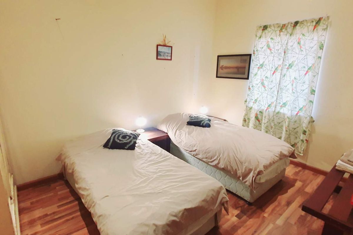 A compact bedroom featuring laminate flooring and a window, currently set up with twin beds.