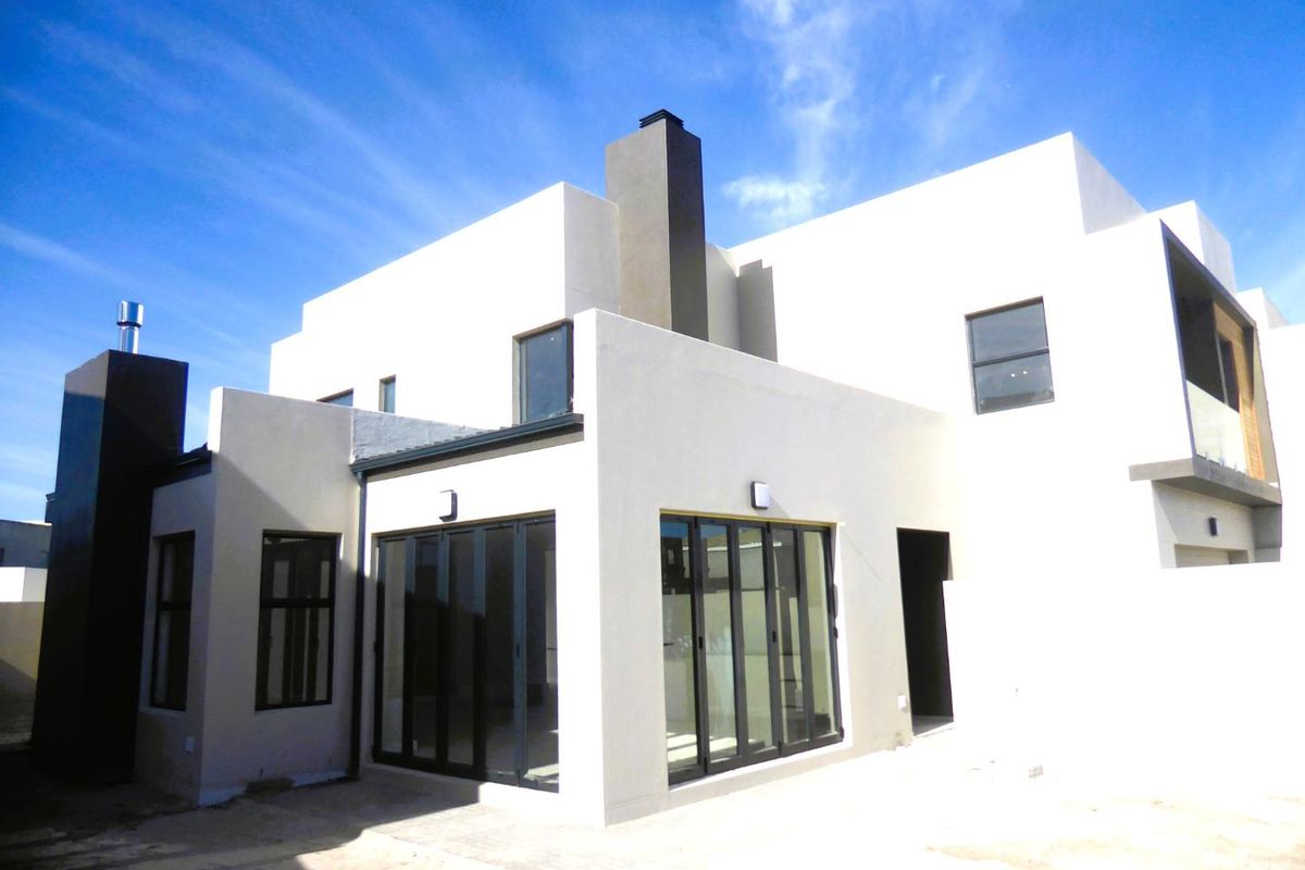 Modern rear elevation of a contemporary house featuring clean lines, large bi-fold doors, a prominent chimney, and a balcony with glass balustrade.