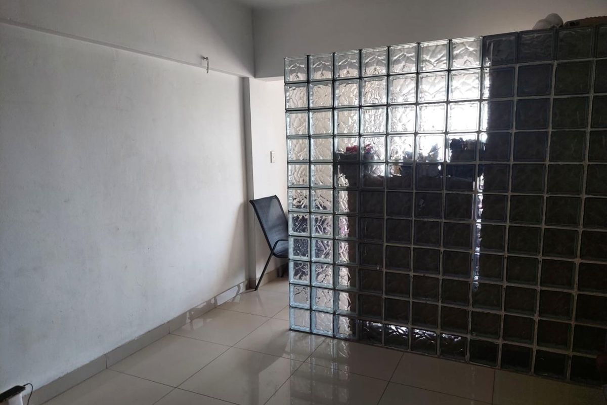 An empty living area featuring a distinctive glass block partition wall and neutral ceramic floor tiles, offering a blank canvas for interior design.
