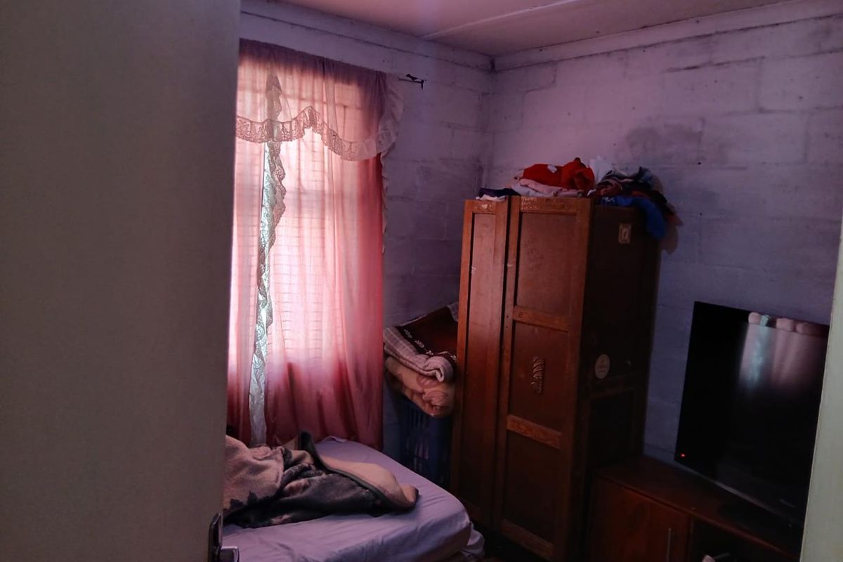 A compact bedroom featuring exposed blockwork walls and a window with curtains, requiring cosmetic updates to improve the overall finish and aesthetic appeal.