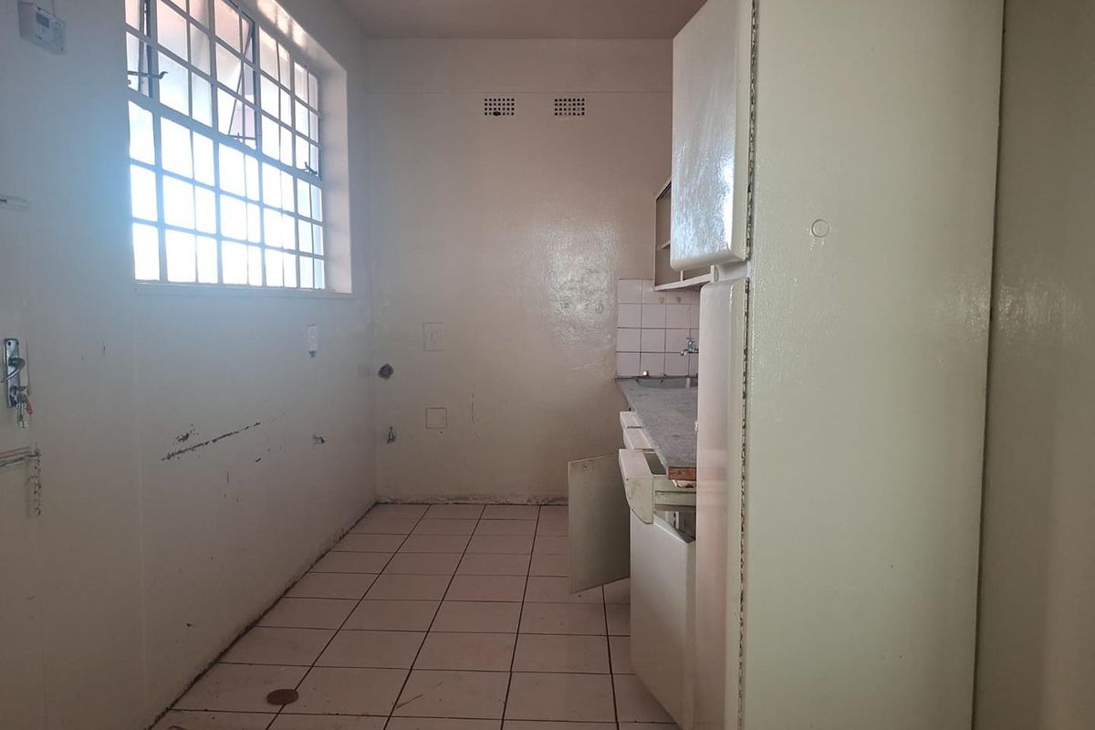 A dated, empty kitchen featuring tiled flooring, a steel window, and basic built-in cabinetry requiring renovation and cosmetic updates.