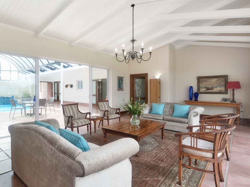Spacious living room featuring vaulted ceilings with exposed beams, tiled flooring, and large sliding glass doors providing seamless access to the outdoor pool area.