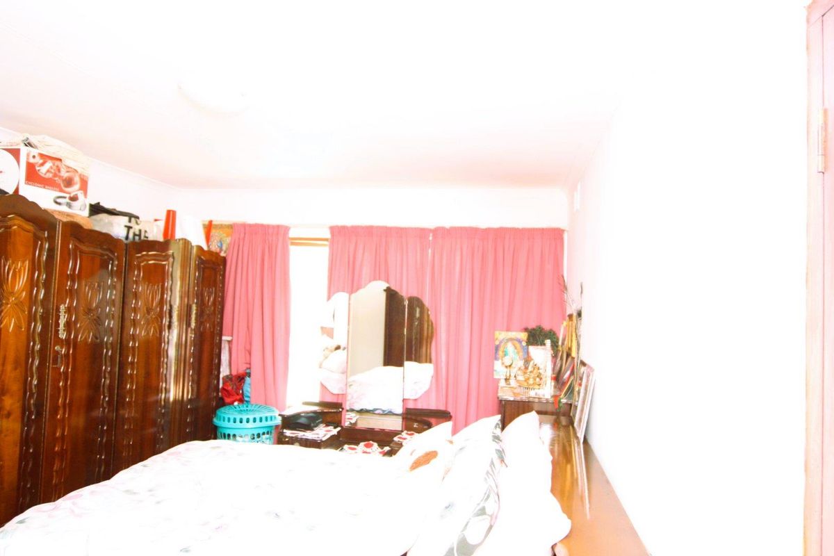 A bedroom featuring built-in wooden cabinetry and pink curtains, currently cluttered with personal items and suffering from significant overexposure.