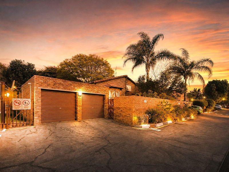 Front exterior view of a townhouse featuring a double garage with roller shutter doors, brick facade, and paved driveway at sunset.
