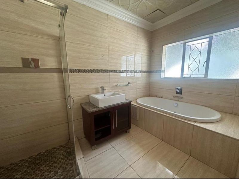 A well-maintained bathroom featuring a glass-enclosed shower, a vessel sink vanity, and a built-in bathtub with neutral wall and floor tiling.