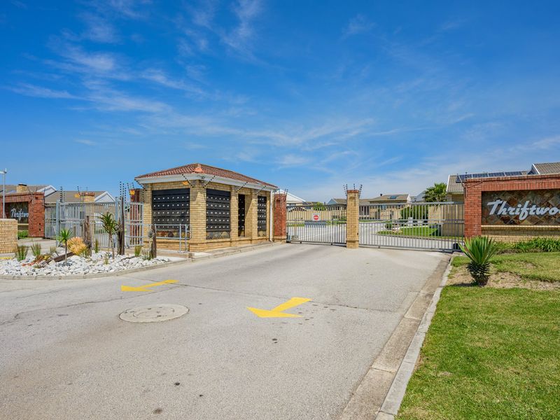 The secure entrance to Thriftwood estate featuring a gated access point, brick security guard house with integrated post boxes, and manicured landscaping.