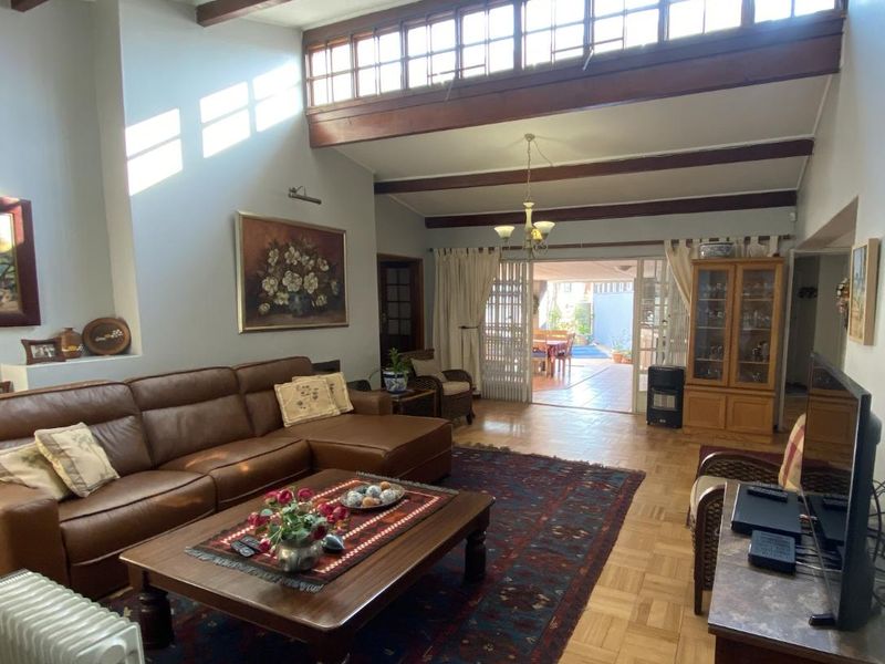 Spacious living room featuring high ceilings with exposed timber beams, clerestory windows for natural light, parquet flooring, and folding doors leading to an outdoor area.