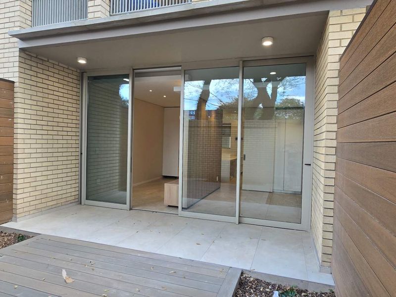 A modern ground-floor patio featuring timber decking, tiled flooring, and large sliding glass doors providing seamless access to the interior living space.