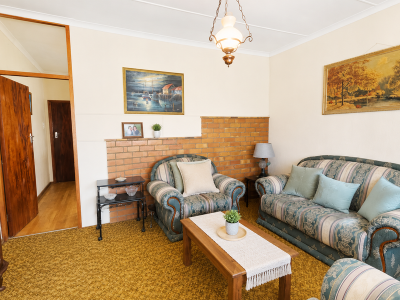 A living room featuring an exposed brick accent wall, timber door, and carpet flooring, offering a traditional layout with potential for modern updates.