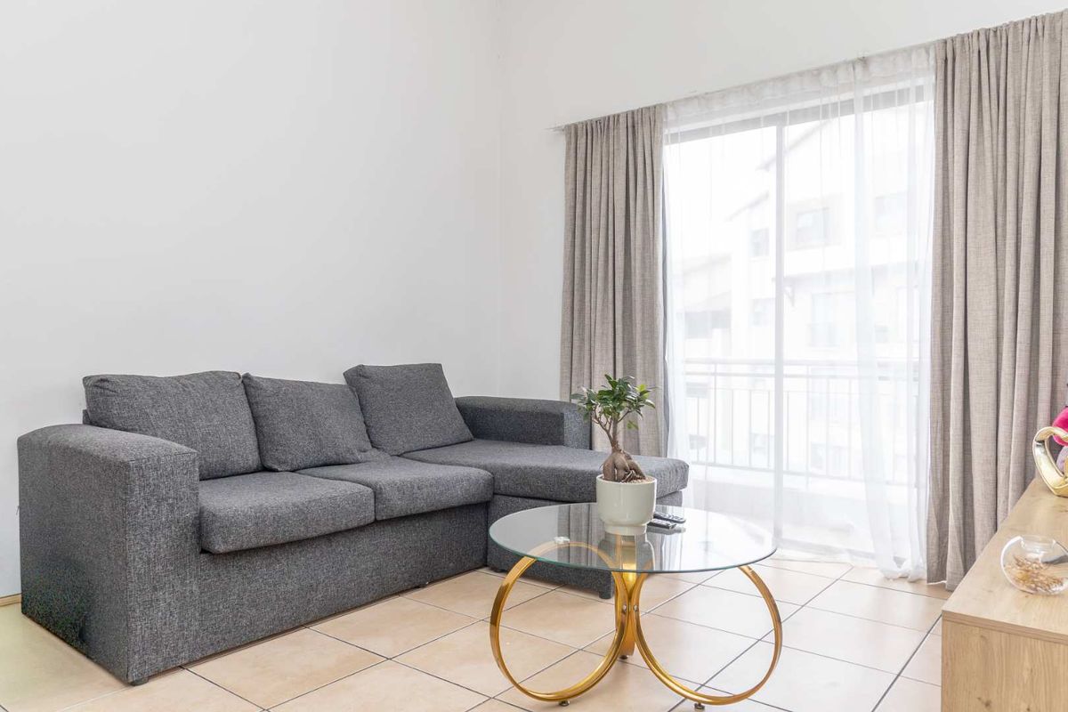 A bright living room featuring tiled flooring and a large sliding glass door that provides access to a private balcony.