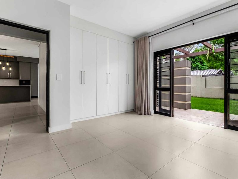 Spacious bedroom featuring neutral tiled flooring, extensive built-in cupboards, and direct access to a private patio area through sliding glass doors.