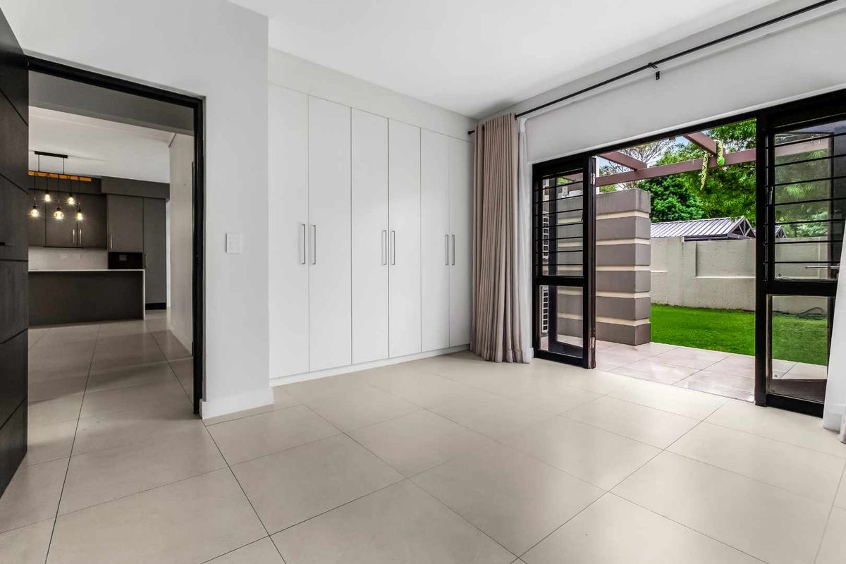 Spacious bedroom featuring neutral tiled flooring, extensive built-in cupboards, and direct access to a private patio area through sliding glass doors.