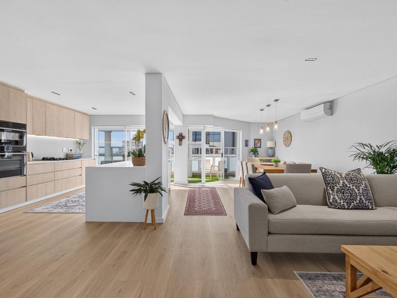 Spacious open-plan living area featuring a modern kitchen with integrated appliances, light wood cabinetry, and seamless flow to a balcony through sliding glass doors.