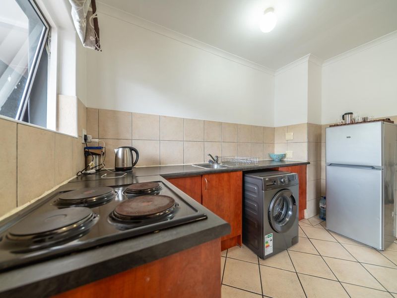 Functional kitchen featuring built-in cabinetry, laminate countertops, an electric hob, and tiled finishes, offering a practical layout for daily use.