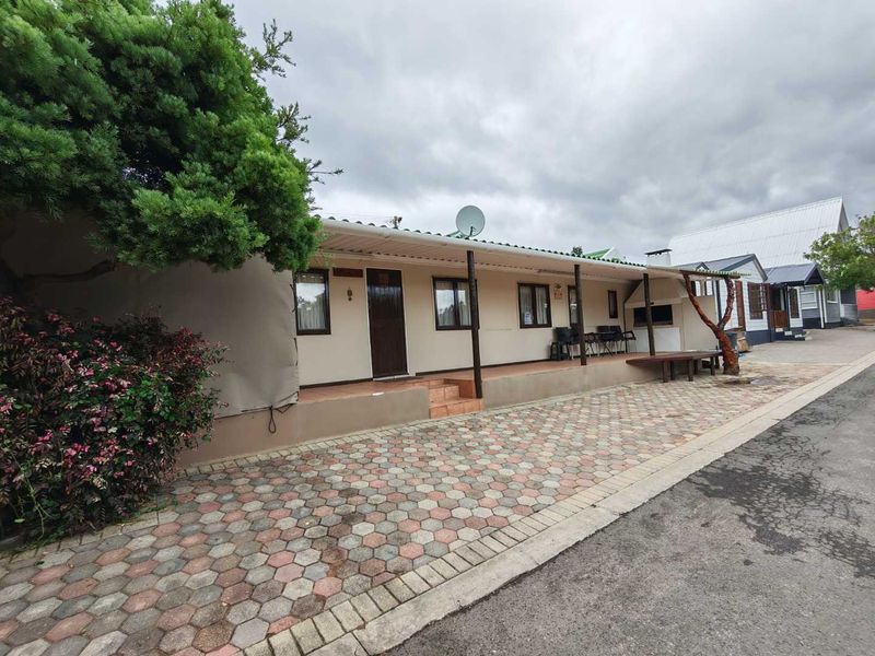 Front exterior view of a single-story residence featuring a covered patio, built-in braai area, and paved driveway.