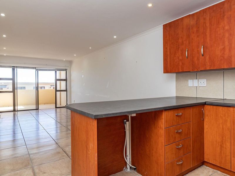 Open-plan kitchen and living area featuring wooden cabinetry, built-in oven, gas hob, tiled flooring, and sliding doors leading to a balcony.