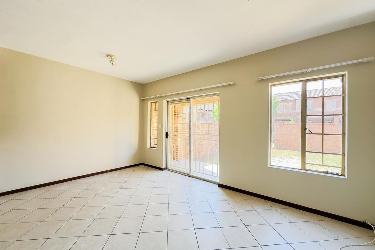A spacious, empty living area featuring neutral tiled flooring, large windows with security bars, and a sliding glass door providing access to the exterior.