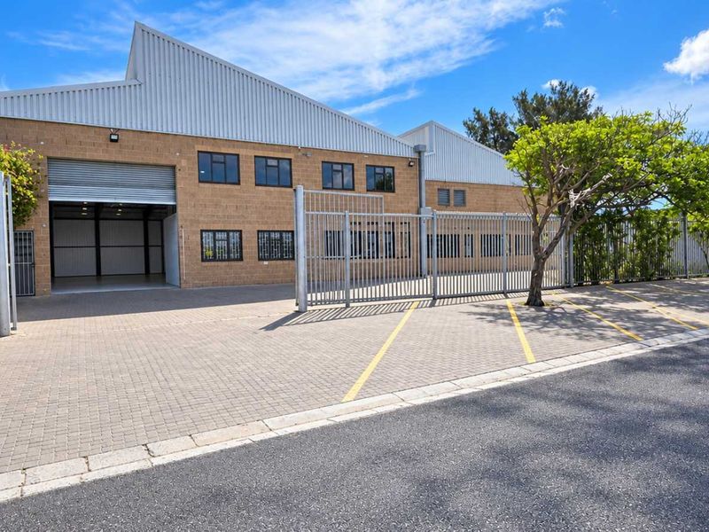 Front view of an industrial property featuring a paved driveway, secure perimeter fencing, and a large roller shutter door for vehicle access.