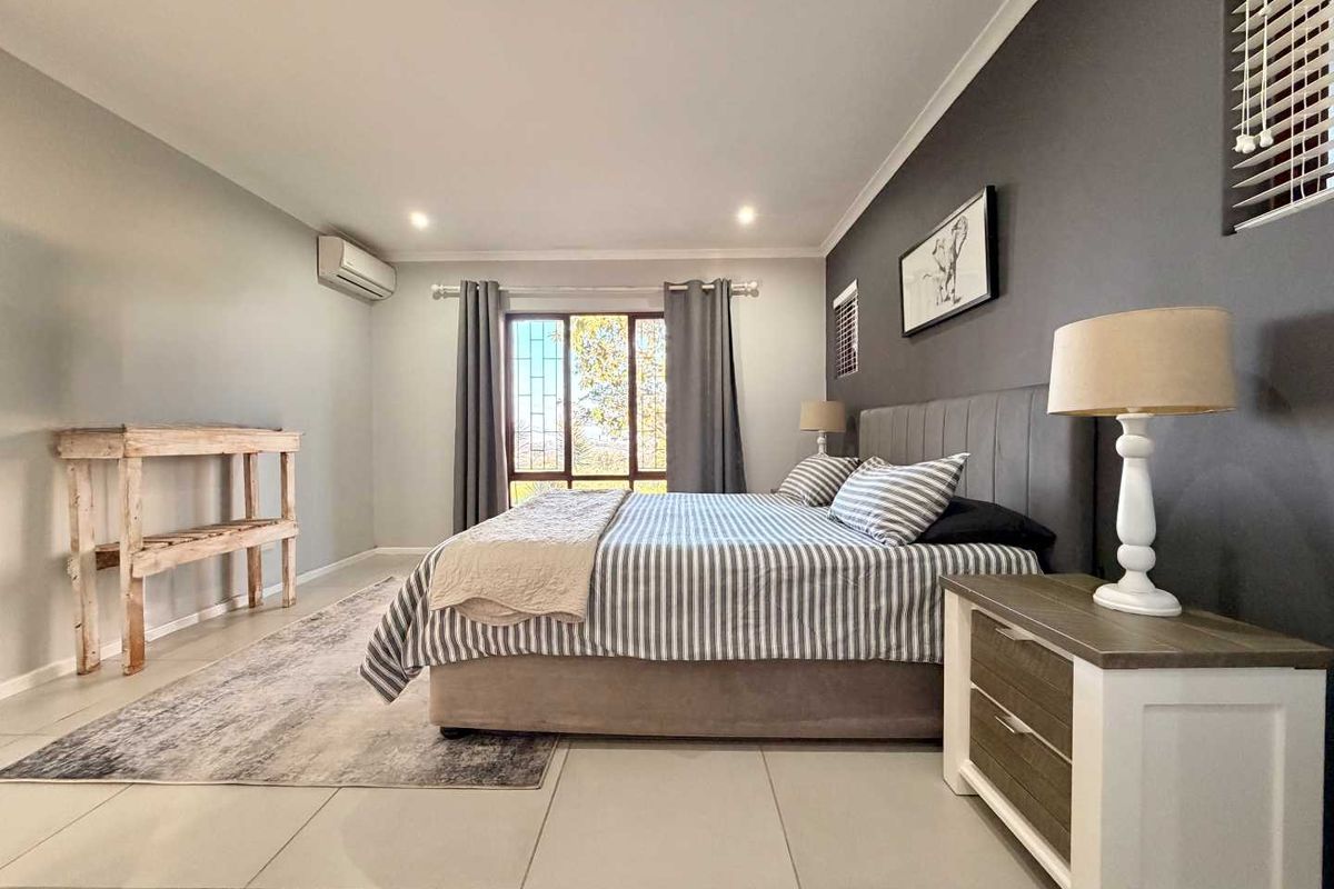 Spacious bedroom featuring neutral tiled flooring, a dark accent wall, recessed downlighting, and a wall-mounted air conditioning unit.