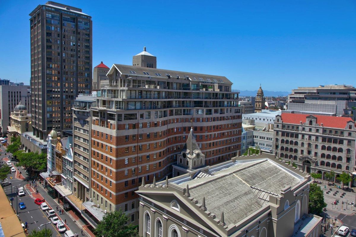 An elevated aerial view of a multi-story apartment building situated in a dense urban city center, showcasing its architectural facade and surrounding cityscape.