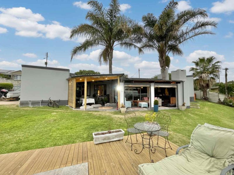Rear view of the property featuring a covered patio area, timber decking, and a well-maintained garden with mature palm trees.