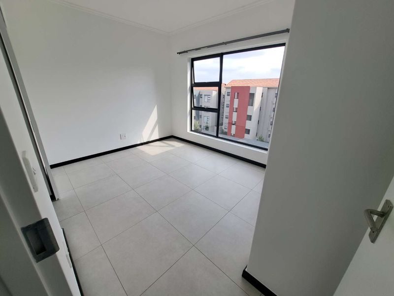 A bright, empty bedroom featuring neutral tiled flooring and large aluminium-framed windows, offering a clean and modern blank canvas.