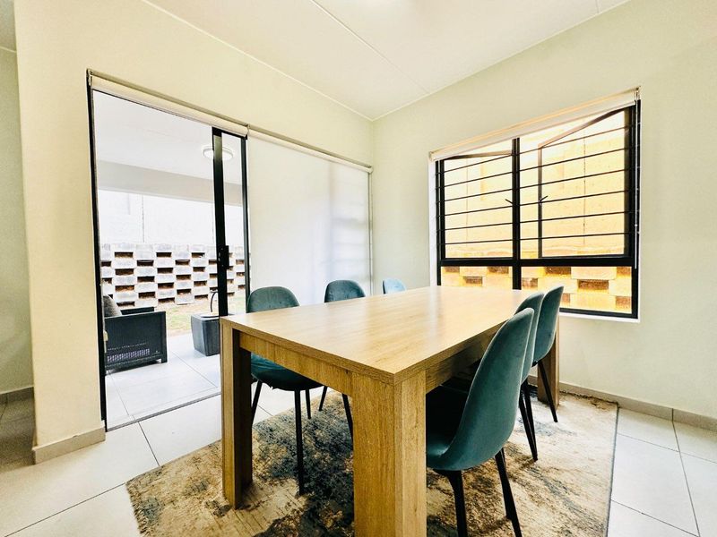 A bright dining room featuring tiled flooring, a large sliding door leading to the patio, and a window with security bars.