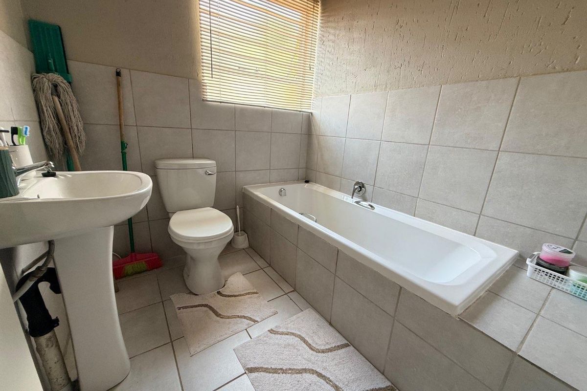 A functional bathroom featuring a pedestal basin, standard toilet, and a built-in bathtub with tiled surround and window blinds.
