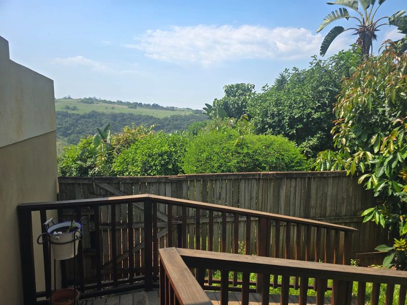 An elevated timber deck featuring a wooden balustrade and fence, offering scenic views of the surrounding landscape and lush greenery.