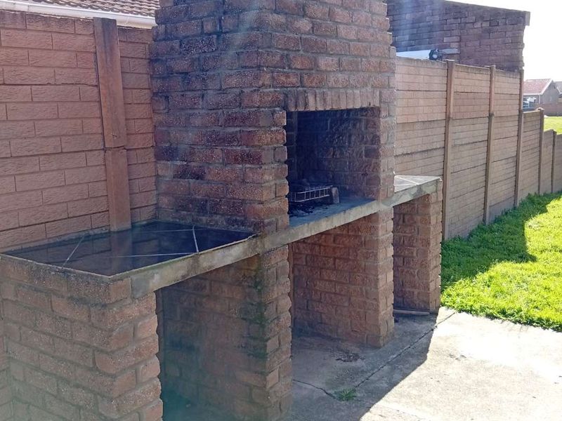 Outdoor patio area featuring a large built-in brick braai with tiled prep surfaces, set against a precast concrete boundary wall.