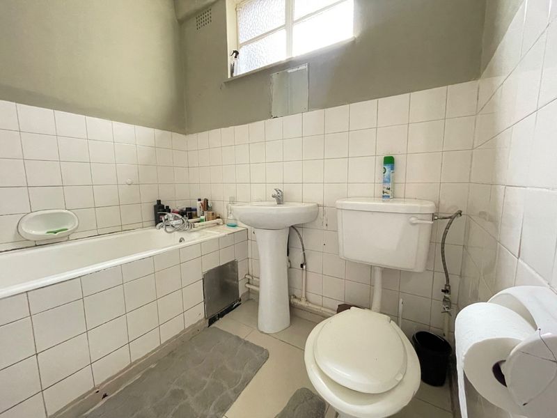 A dated bathroom featuring a pedestal basin, bathtub, and toilet with white wall tiling. The space requires modernization of fixtures and finishes.