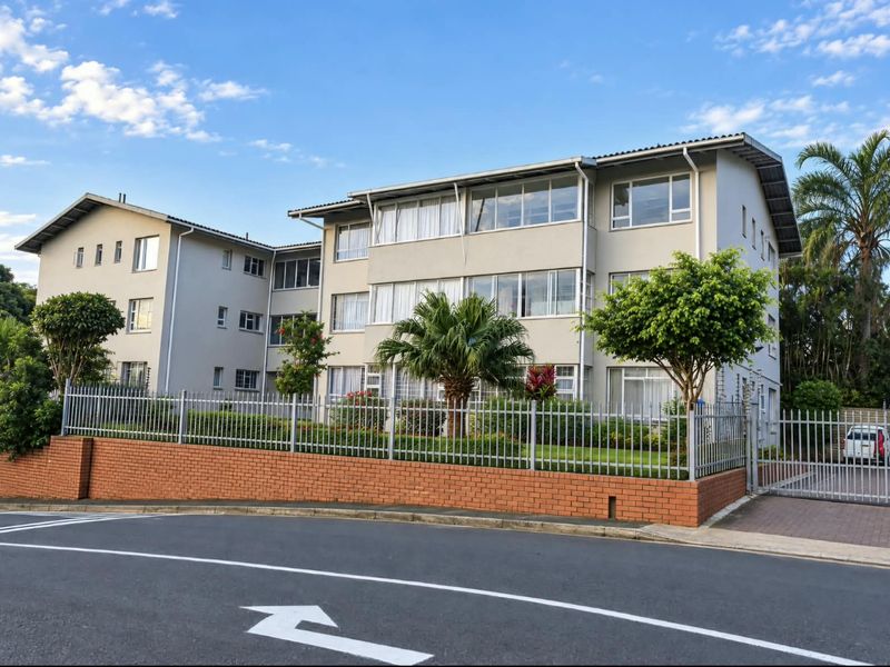 A well-maintained multi-story apartment complex featuring a brick boundary wall, secure gated entrance, and landscaped garden area viewed from the street.