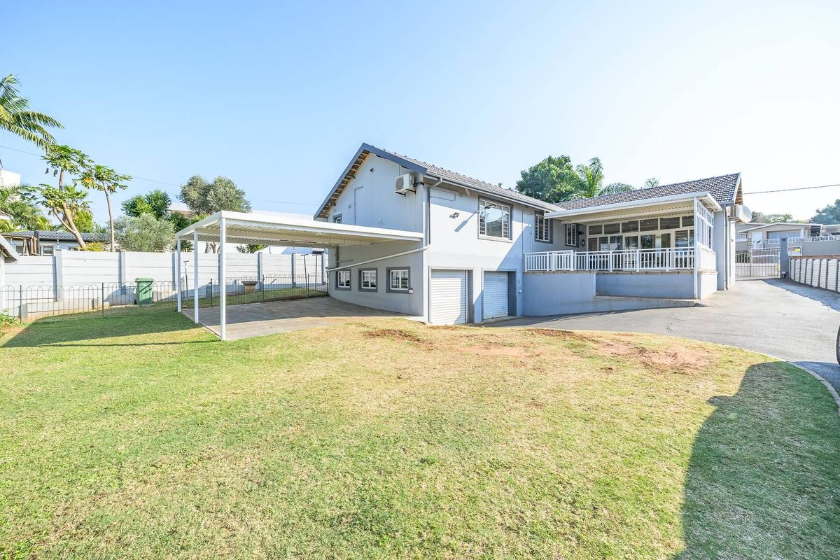 Rear view of the property featuring a paved driveway, carport, integrated garage, and an elevated patio area with white railings.
