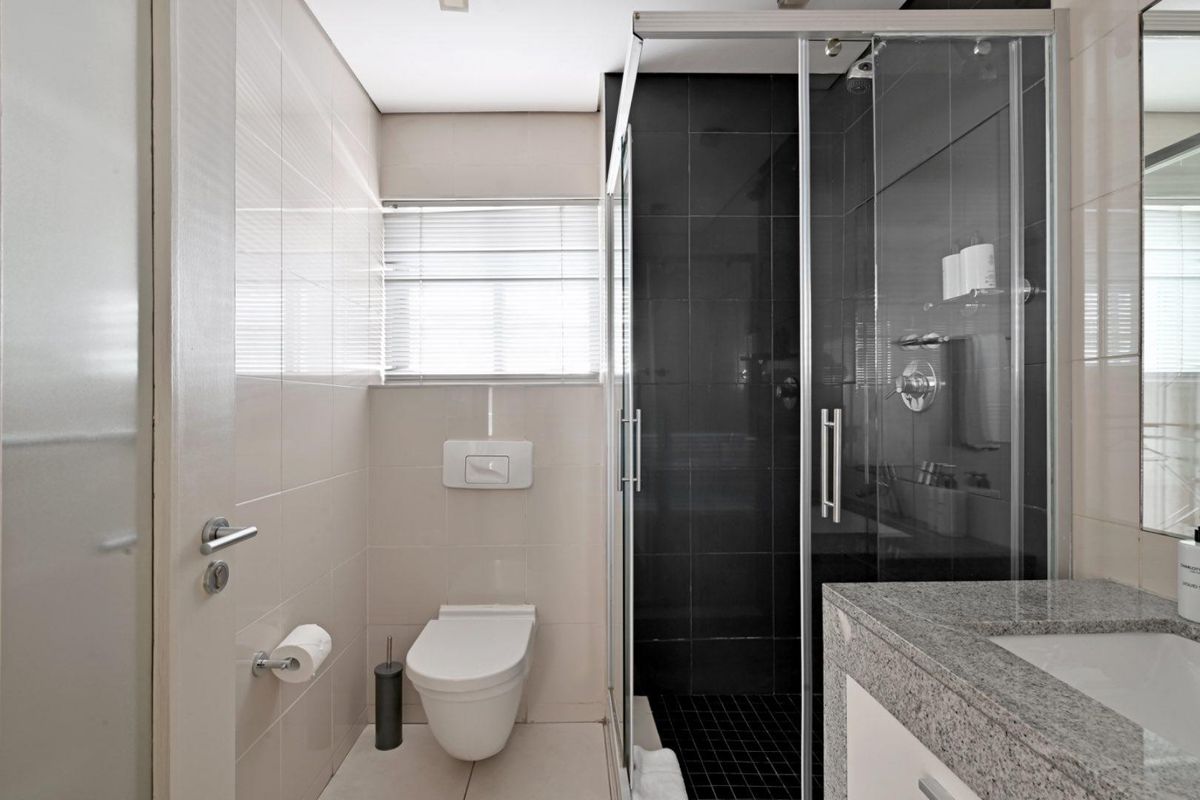 Modern bathroom featuring a glass-enclosed shower, wall-hung toilet, and a granite-topped vanity with neutral wall tiling.