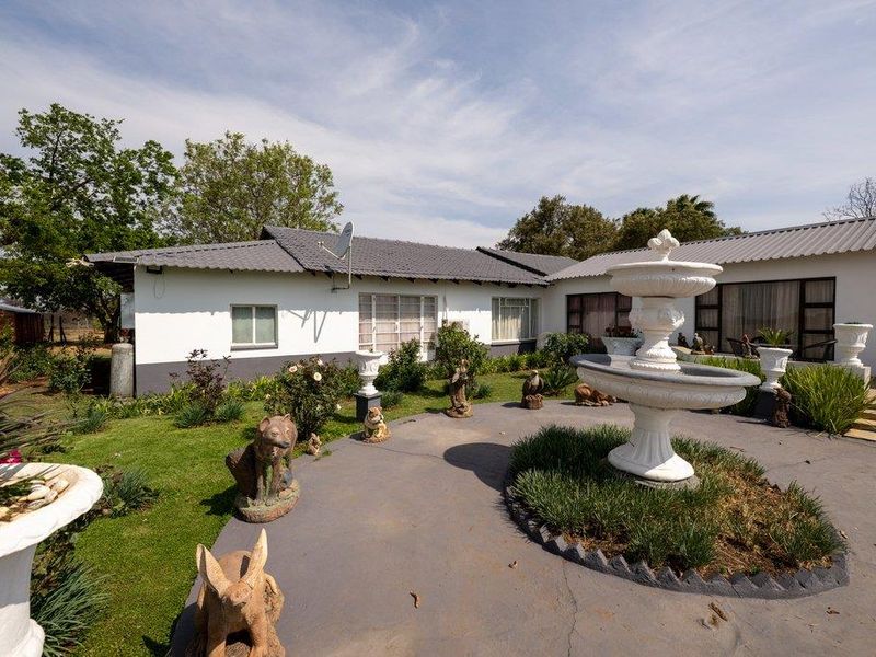 Rear view of the farmhouse featuring a paved patio area, a central stone fountain, and a well-maintained garden with a tiled roof structure.