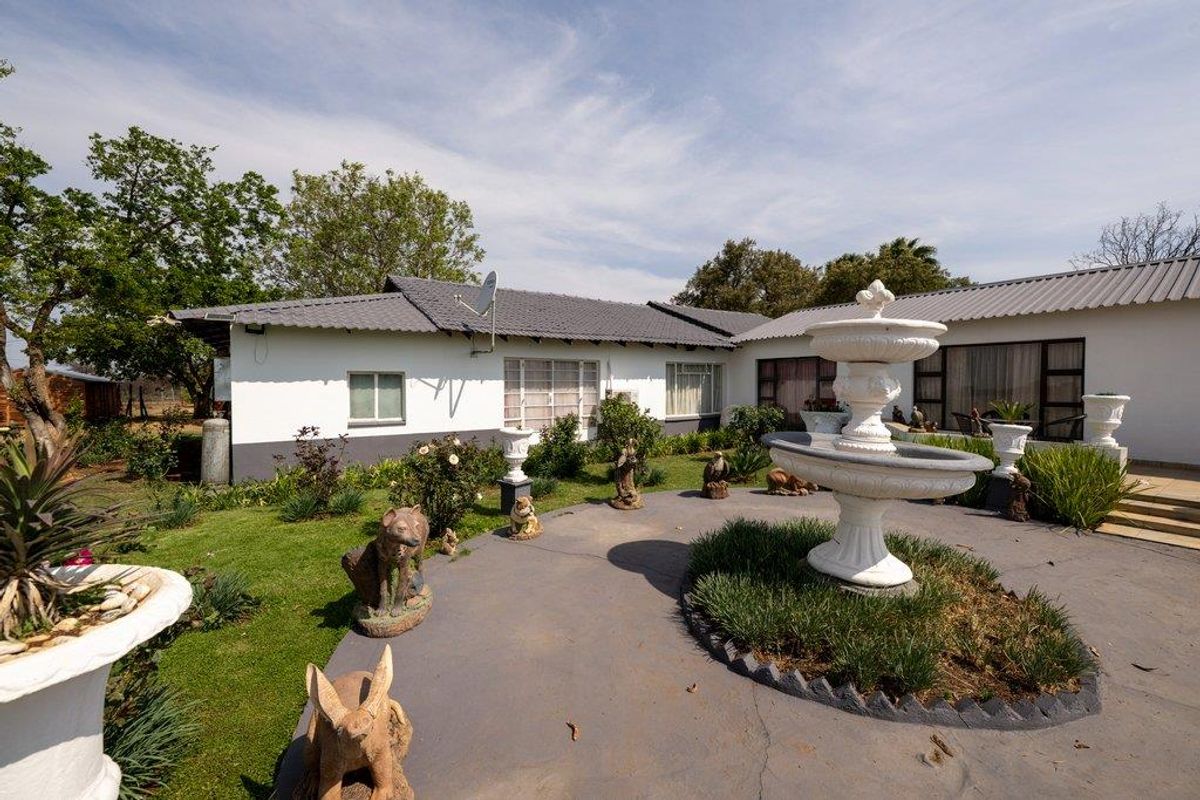 Rear view of the farmhouse featuring a paved patio area, a central stone fountain, and a well-maintained garden with a tiled roof structure.
