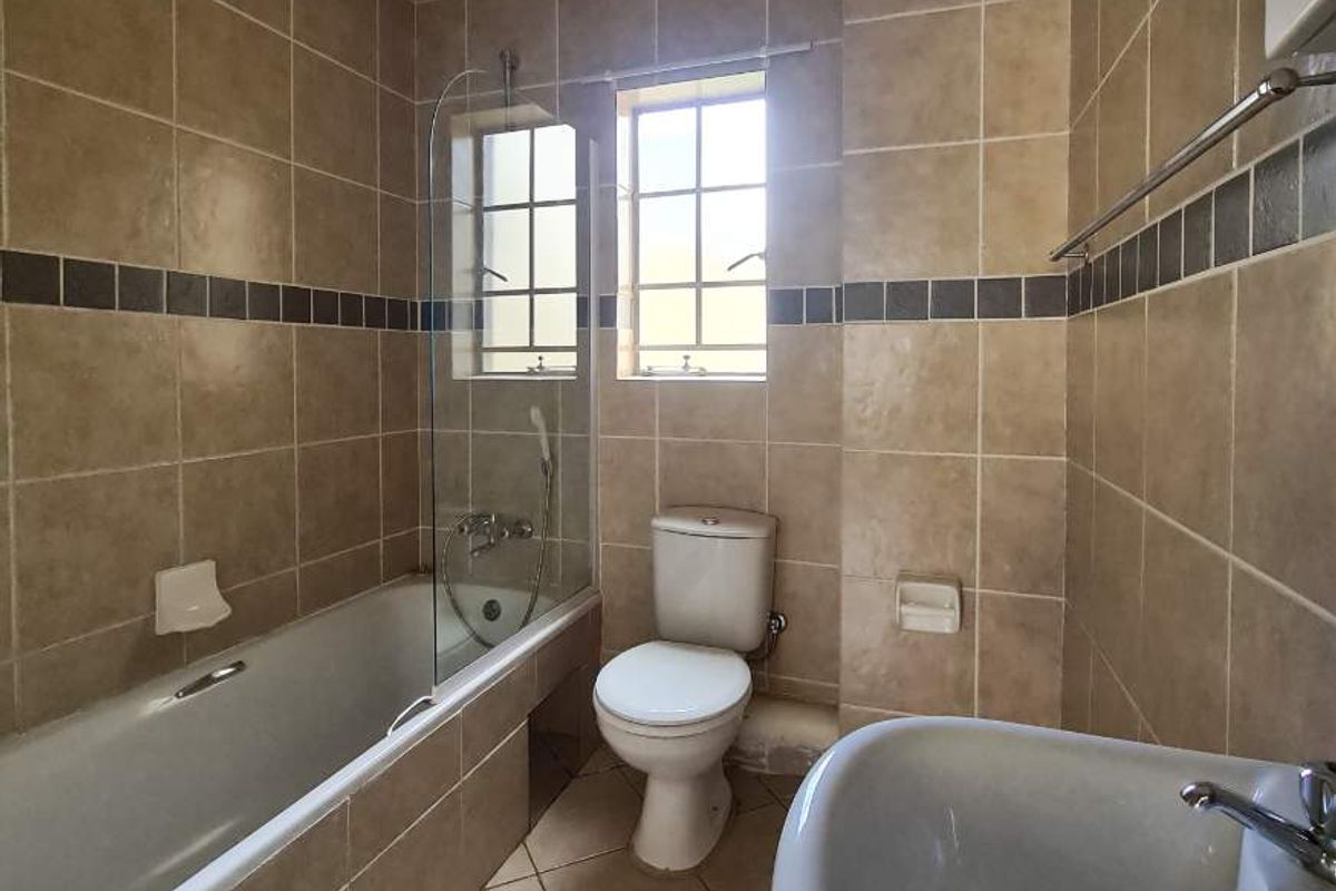 A functional bathroom featuring a bathtub with a glass screen, pedestal basin, and neutral wall and floor tiling.
