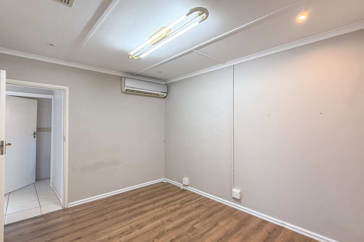 An empty bedroom featuring wood-look laminate flooring, a wall-mounted air conditioning unit, and a doorway leading to an adjacent tiled space.