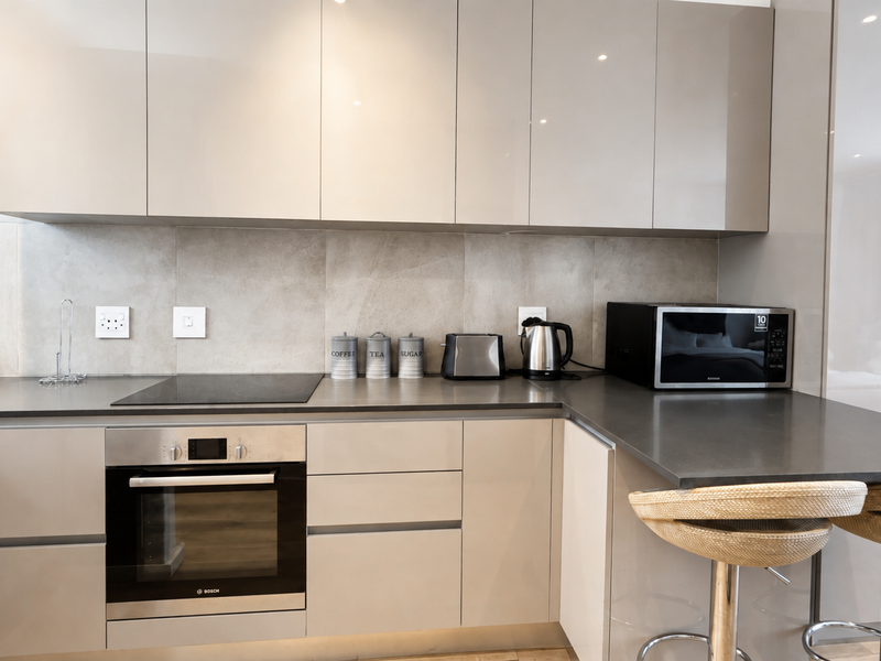 Modern kitchen featuring sleek gloss cabinetry, stone countertops, built-in oven, electric hob, and integrated microwave with a contemporary tiled backsplash.
