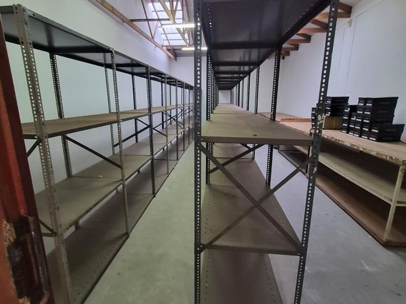 A functional utility or storage space featuring exposed timber roof trusses, skylights, and durable concrete flooring, suitable for various commercial storage needs.