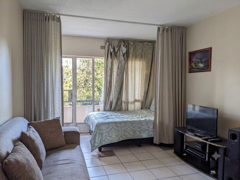 Open-plan living area featuring tiled flooring and direct access to a balcony through a sliding glass door with security gate.