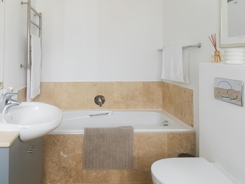 A clean, modern bathroom featuring a built-in bathtub with travertine tiling, a wall-mounted basin, and a concealed cistern toilet.