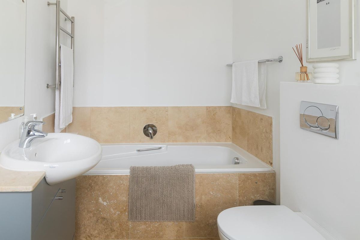 A clean, modern bathroom featuring a built-in bathtub with travertine tiling, a wall-mounted basin, and a concealed cistern toilet.