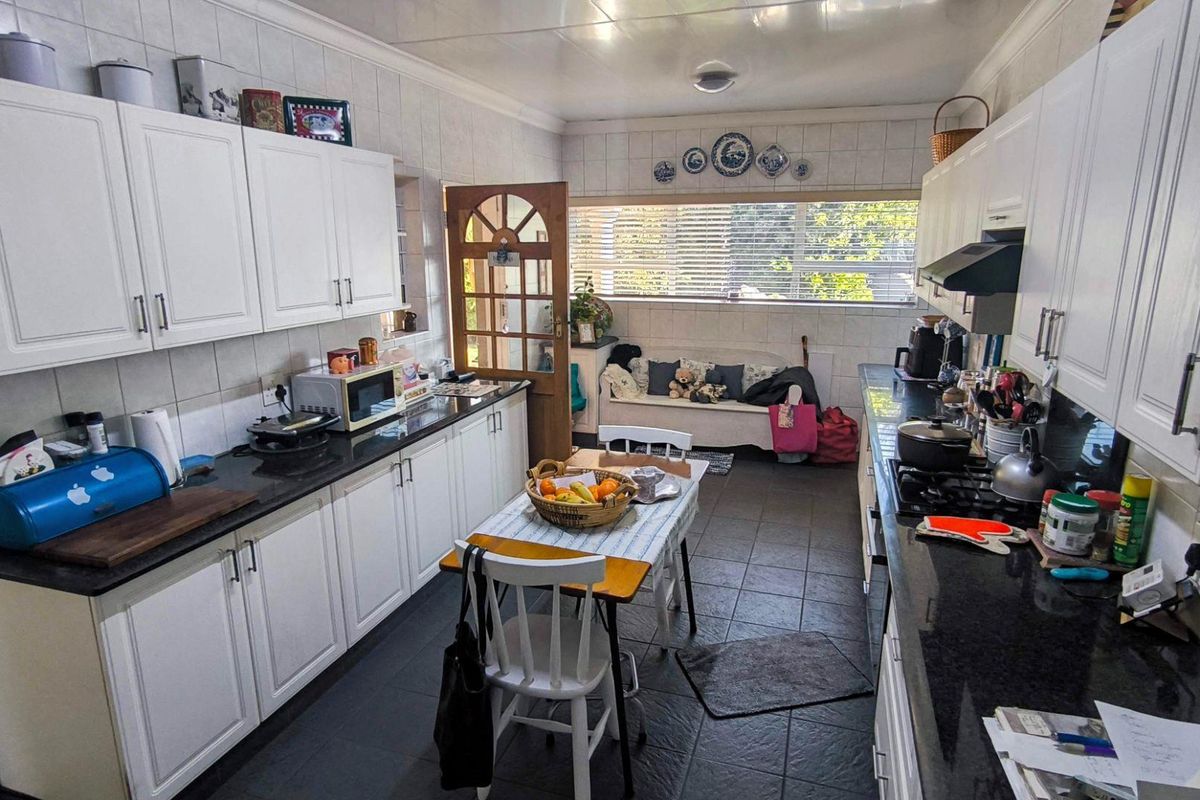 A functional galley-style kitchen featuring white cabinetry, dark granite countertops, gas hob, and tiled finishes throughout.
