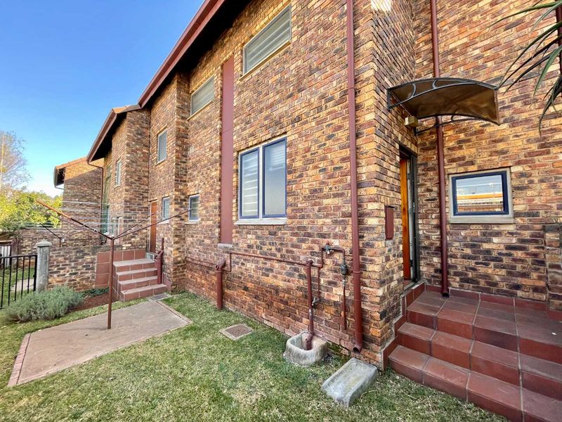 Rear exterior view of the townhouse featuring face brick construction, tiled entrance steps, and a small concrete patio area.