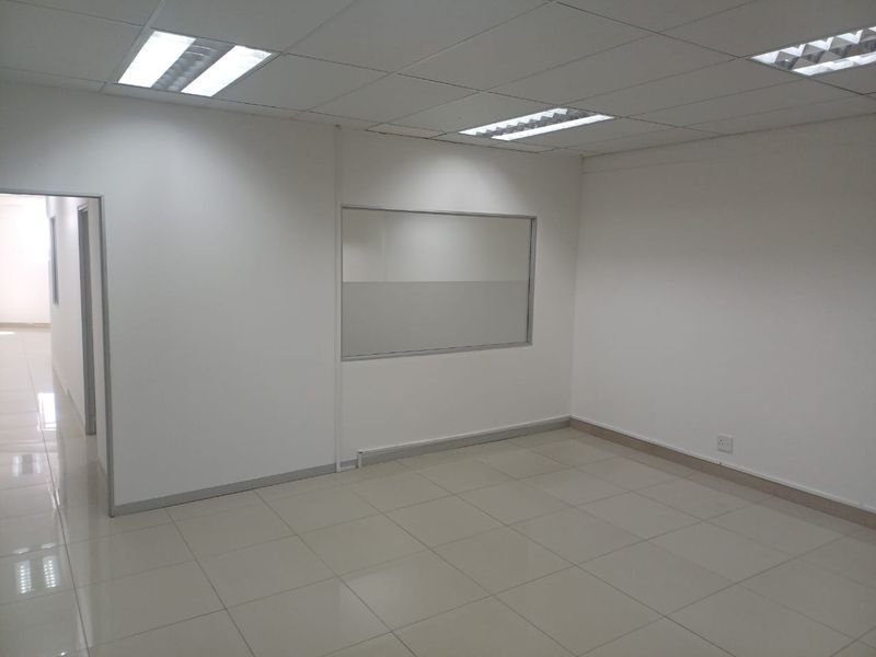 A clean, vacant office space featuring neutral ceramic floor tiles, a suspended ceiling with recessed lighting, and an internal glass partition.