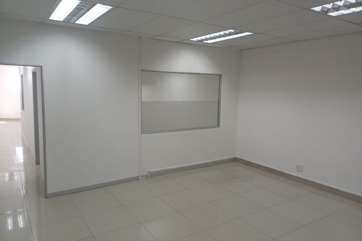 A clean, vacant office space featuring neutral ceramic floor tiles, a suspended ceiling with recessed lighting, and an internal glass partition.